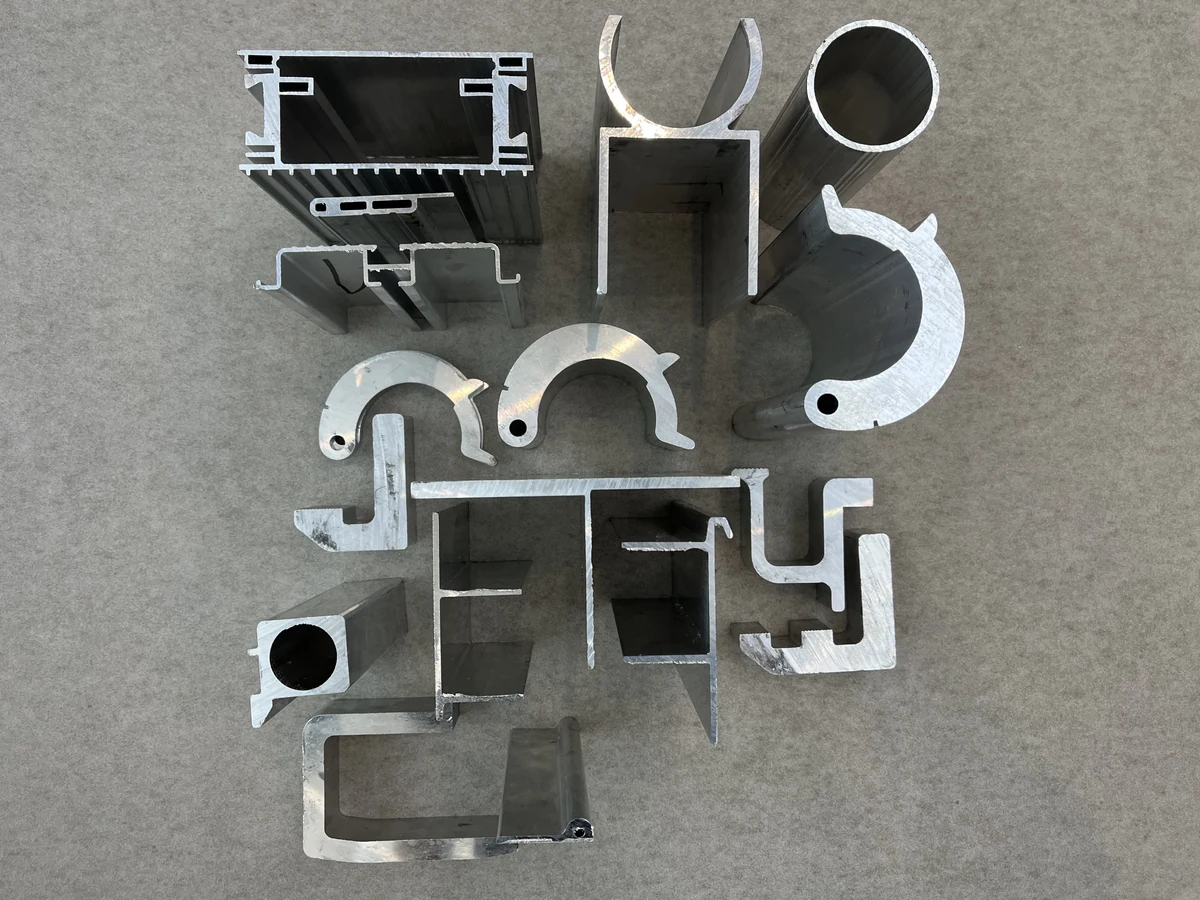 Muster stranggepresster Aluminiumprofile mit hohlen, gebogenen und asymmetrischen Querschnitten auf grauem Hintergrund